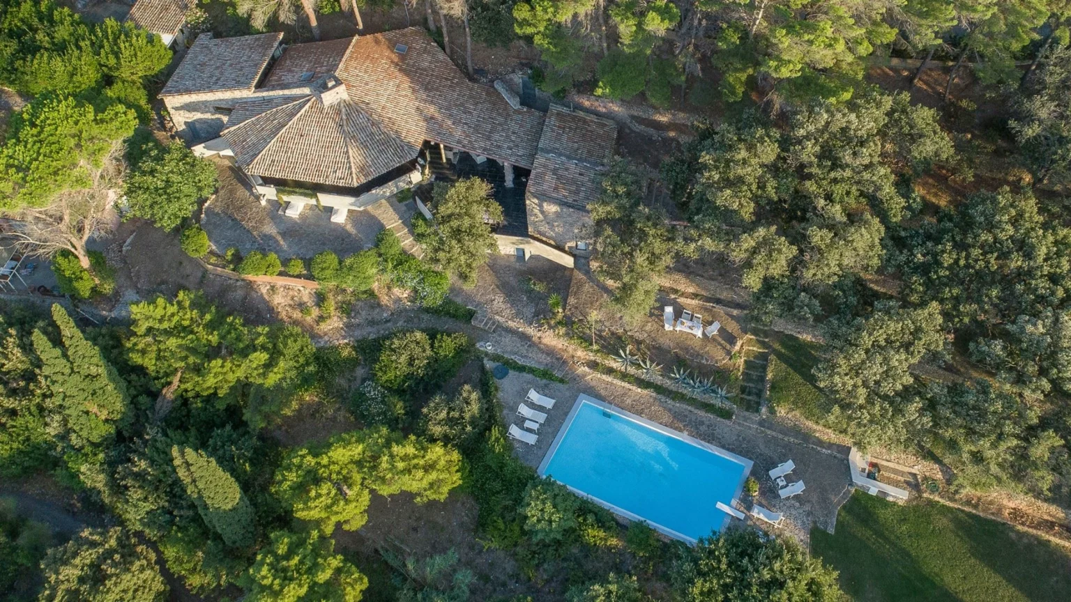 Aerial view of a rustic stone villa surrounded by lush greenery, featuring a sparkling blue swimming pool and outdoor seating areas, ideal for a tranquil getaway. | Only on SopranoVillas