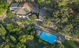 Aerial view of a rustic stone villa surrounded by lush greenery, featuring a sparkling blue swimming pool and outdoor seating areas, ideal for a tranquil getaway.