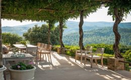 Scenic outdoor patio with wooden furniture, surrounded by lush greenery and mountains in the background, perfect for relaxation and enjoying nature.