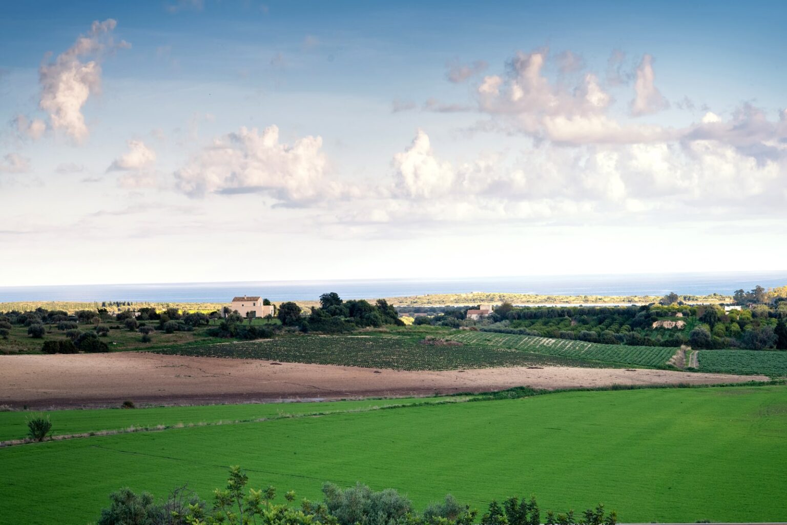 Scenic landscape featuring lush green fields, distant hills, and a clear blue sky with scattered clouds, overlooking a coastline. | Only on SopranoVillas