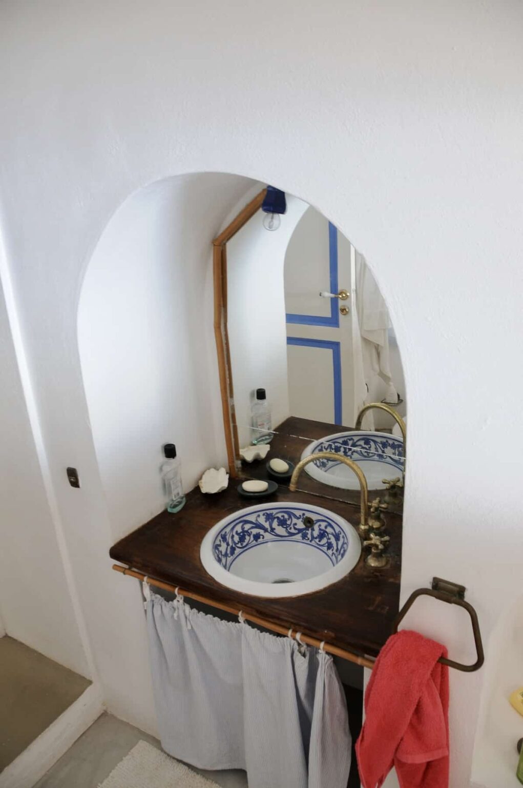Elegant bathroom setting featuring a wooden mirror frame, ornate sink with blue and white ceramic design, and minimalistic decor. The wall is painted white with a blue accent door, creating a serene and stylish atmosphere. | Only on SopranoVillas