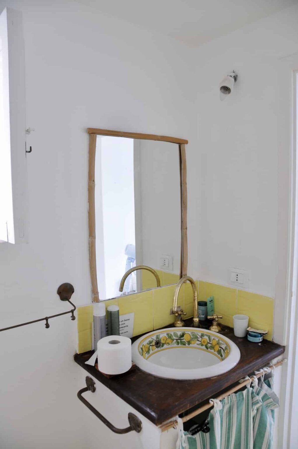 Modern bathroom with a yellow sink, stylish brass faucet, and a large wooden-framed mirror reflecting the bright space. | Only on SopranoVillas