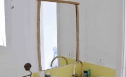 Modern bathroom with a yellow sink, stylish brass faucet, and a large wooden-framed mirror reflecting the bright space.