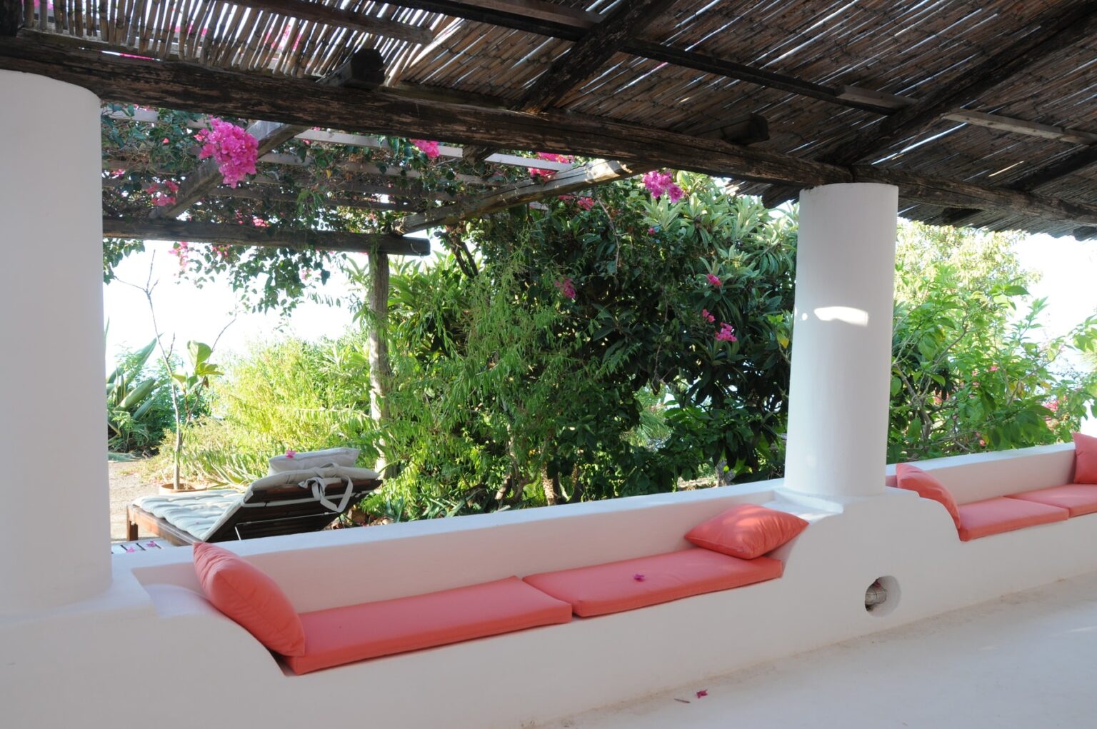 Cozy outdoor seating area with orange cushions under a thatched roof, surrounded by lush greenery and blooming flowers, ideal for relaxation and enjoying nature. | Only on SopranoVillas