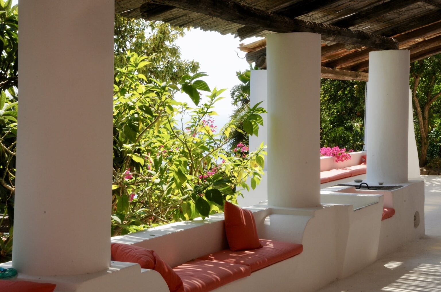 Cozy outdoor seating area with white columns, surrounded by lush greenery and vibrant flowers, offering a tranquil atmosphere for relaxation. | Only on SopranoVillas