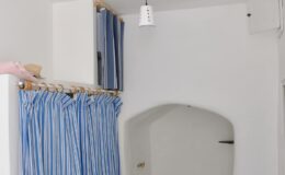 Interior view of a minimalist room featuring blue and white striped curtains, a hanging light fixture, and a small alcove with a stone wall and a faucet, designed for a cozy and functional space.