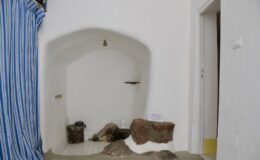Interior view of a minimalist room featuring a white wall with an arched niche, decorative stones, and a blue and white striped curtain, highlighting simple design elements.