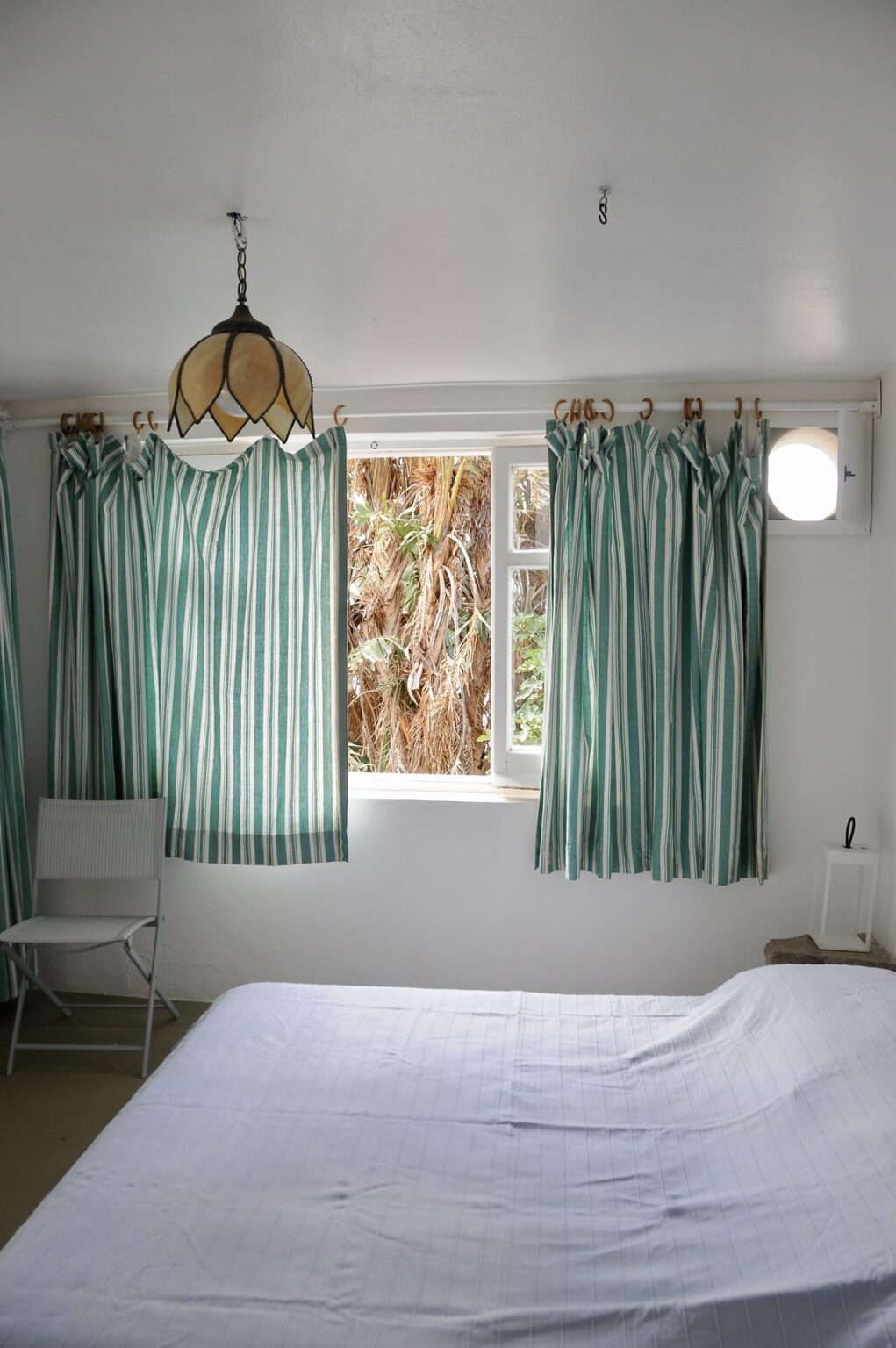 Interior view of a room featuring light green and white striped curtains, a window with natural light, and a minimalistic chair, creating a bright and airy atmosphere. | Only on SopranoVillas