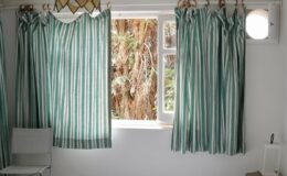 Interior view of a room featuring light green and white striped curtains, a window with natural light, and a minimalistic chair, creating a bright and airy atmosphere.