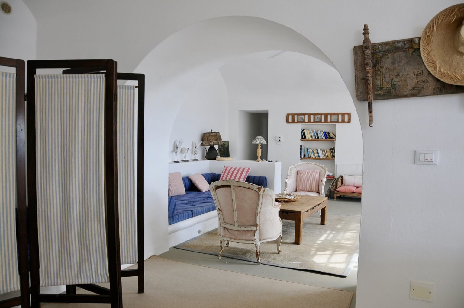 Cozy interior of a modern living room featuring a blue sofa, wicker chairs, decorative wall art, and a light-colored rug, set in a bright, airy space with arched ceilings and a room divider. | Only on SopranoVillas