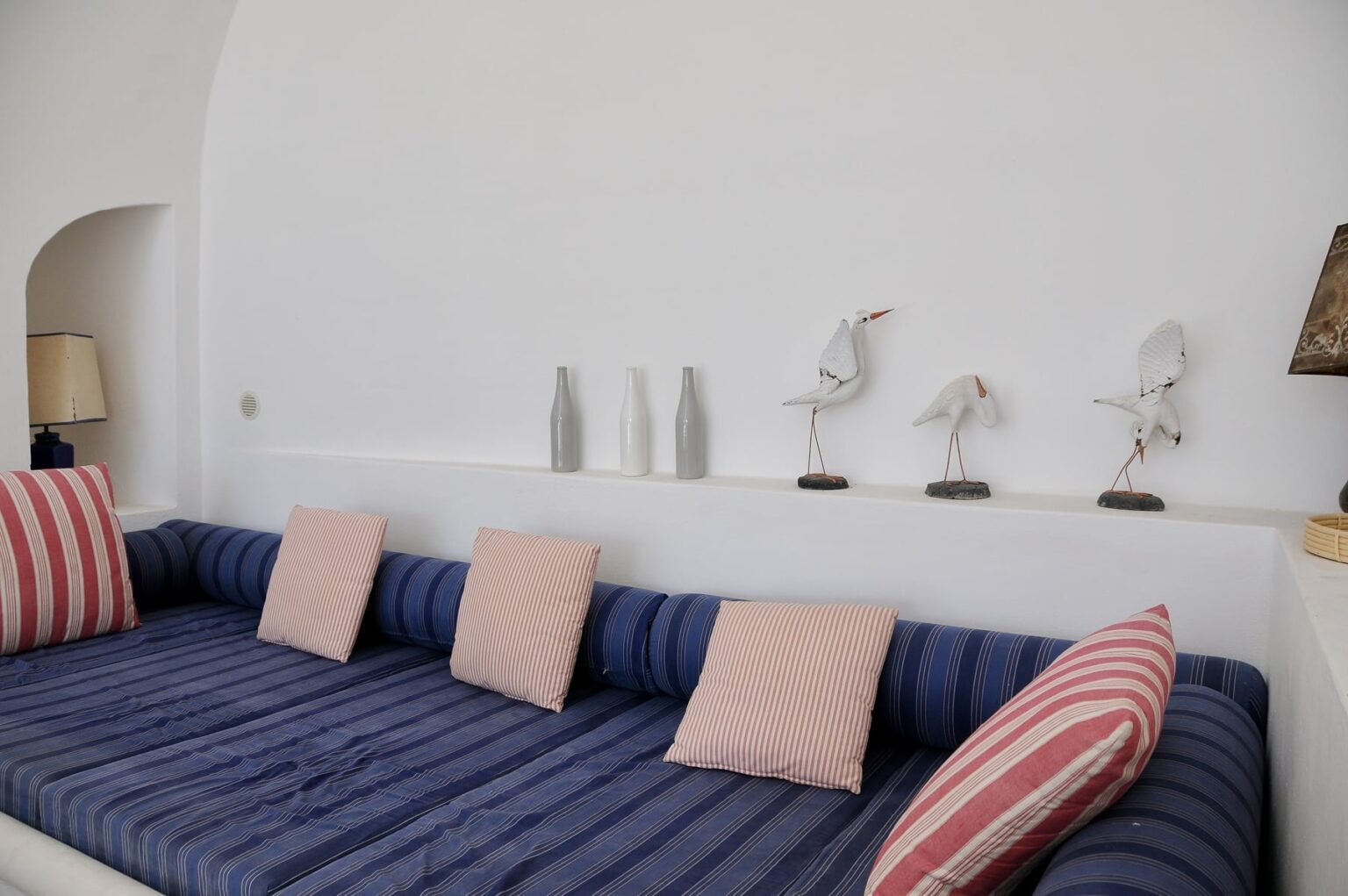 Cozy living room featuring a blue striped sofa with pink cushions, complemented by decorative bird sculptures and minimalist vases on a white wall. | Only on SopranoVillas