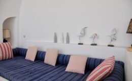 Cozy living room featuring a blue striped sofa with pink cushions, complemented by decorative bird sculptures and minimalist vases on a white wall.