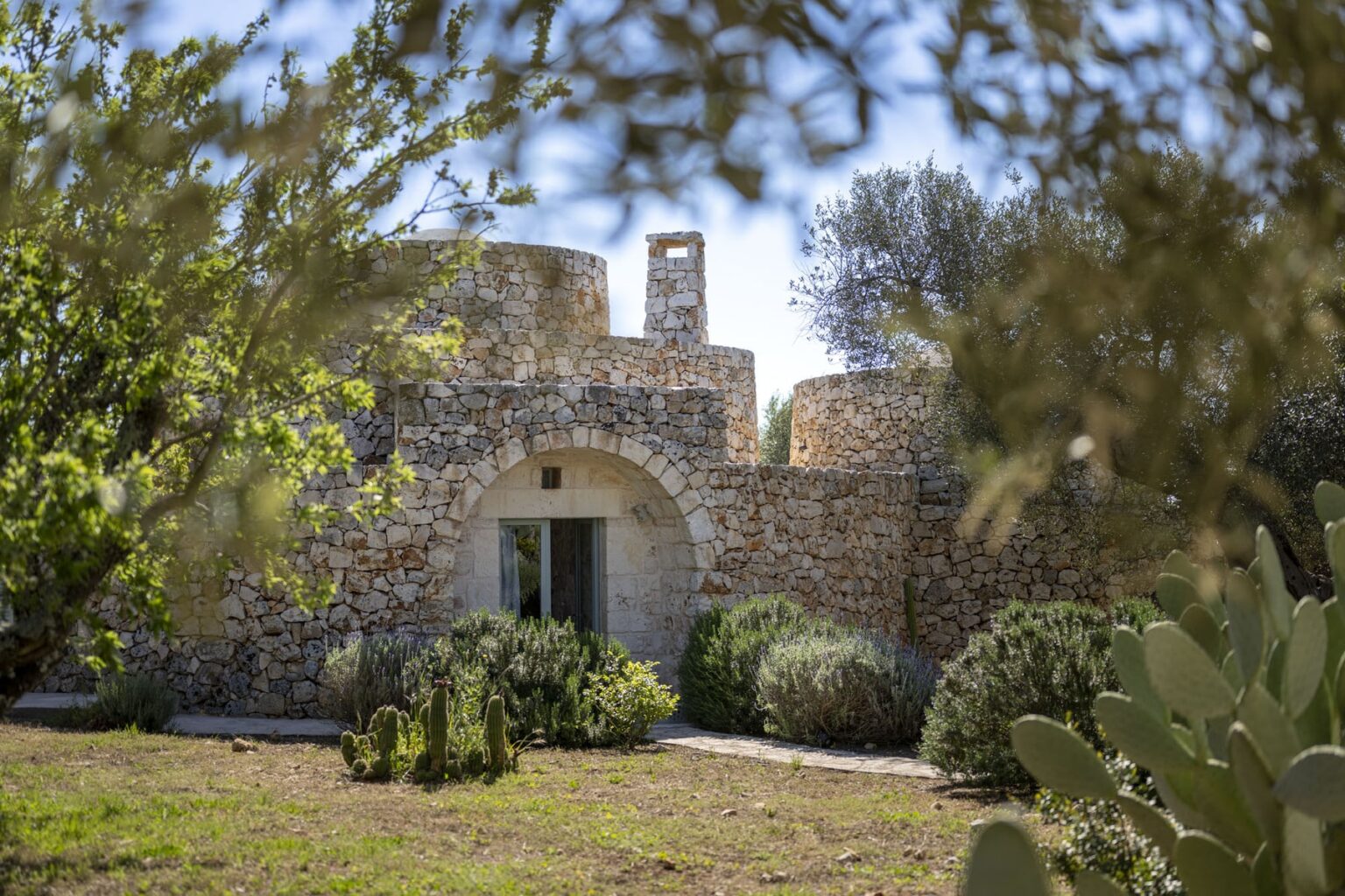 Historic stone building surrounded by lush greenery and cacti, showcasing traditional architecture in a serene outdoor setting. | Only on SopranoVillas
