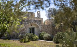 Historic stone building surrounded by lush greenery and cacti, showcasing traditional architecture in a serene outdoor setting.