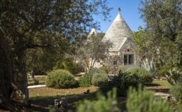 Tranquil landscape featuring a traditional trullo house surrounded by lush greenery and trees, showcasing a serene outdoor setting.