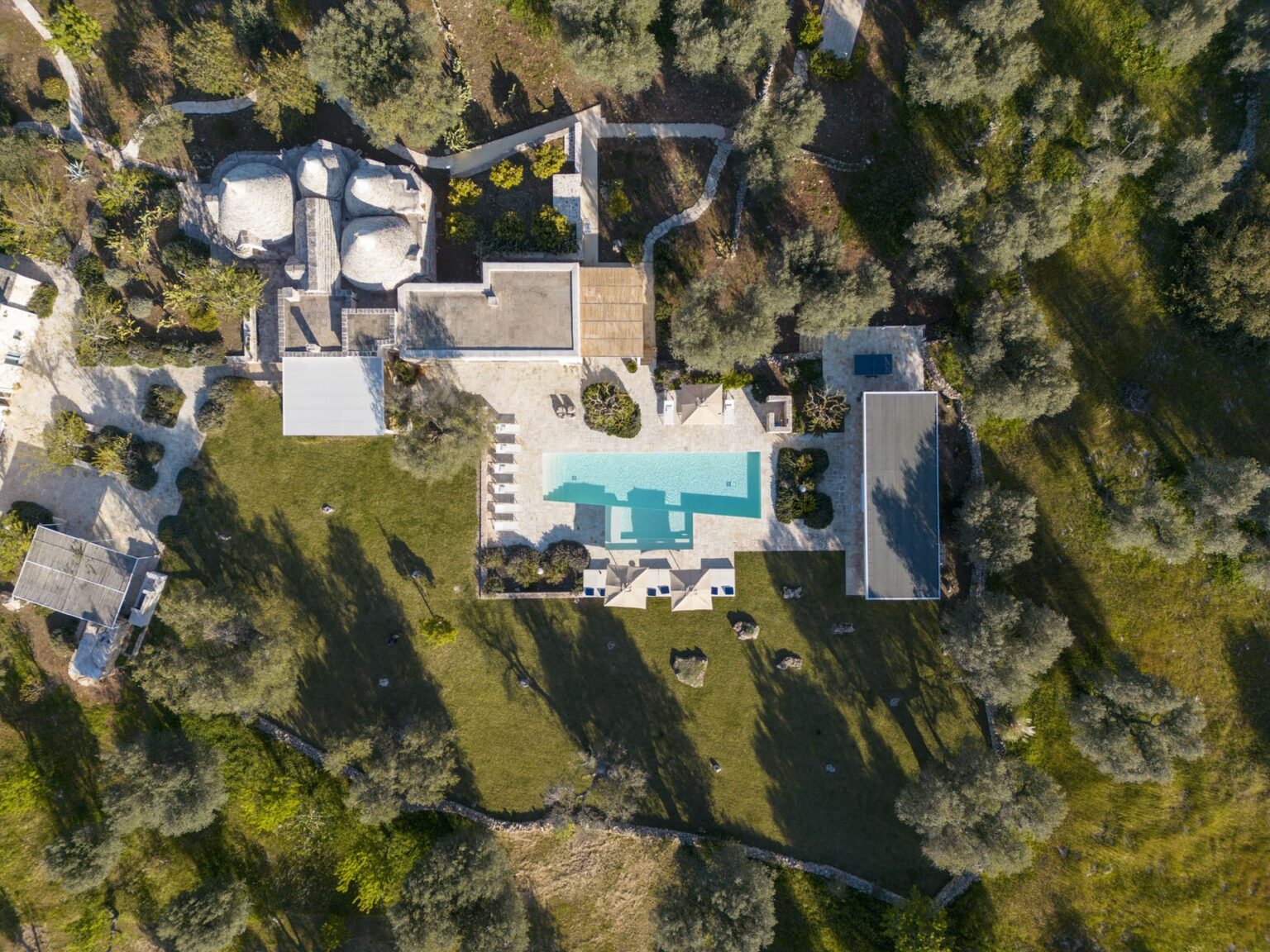 Aerial view of a luxury villa featuring a swimming pool, landscaped gardens, and unique stone structures surrounded by olive trees, ideal for relaxation and outdoor living. | Only on SopranoVillas
