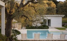Modern villa with a swimming pool surrounded by a landscaped garden and autumn foliage. Elegant outdoor seating area by the pool, featuring sun loungers and a view of the contemporary white architecture.