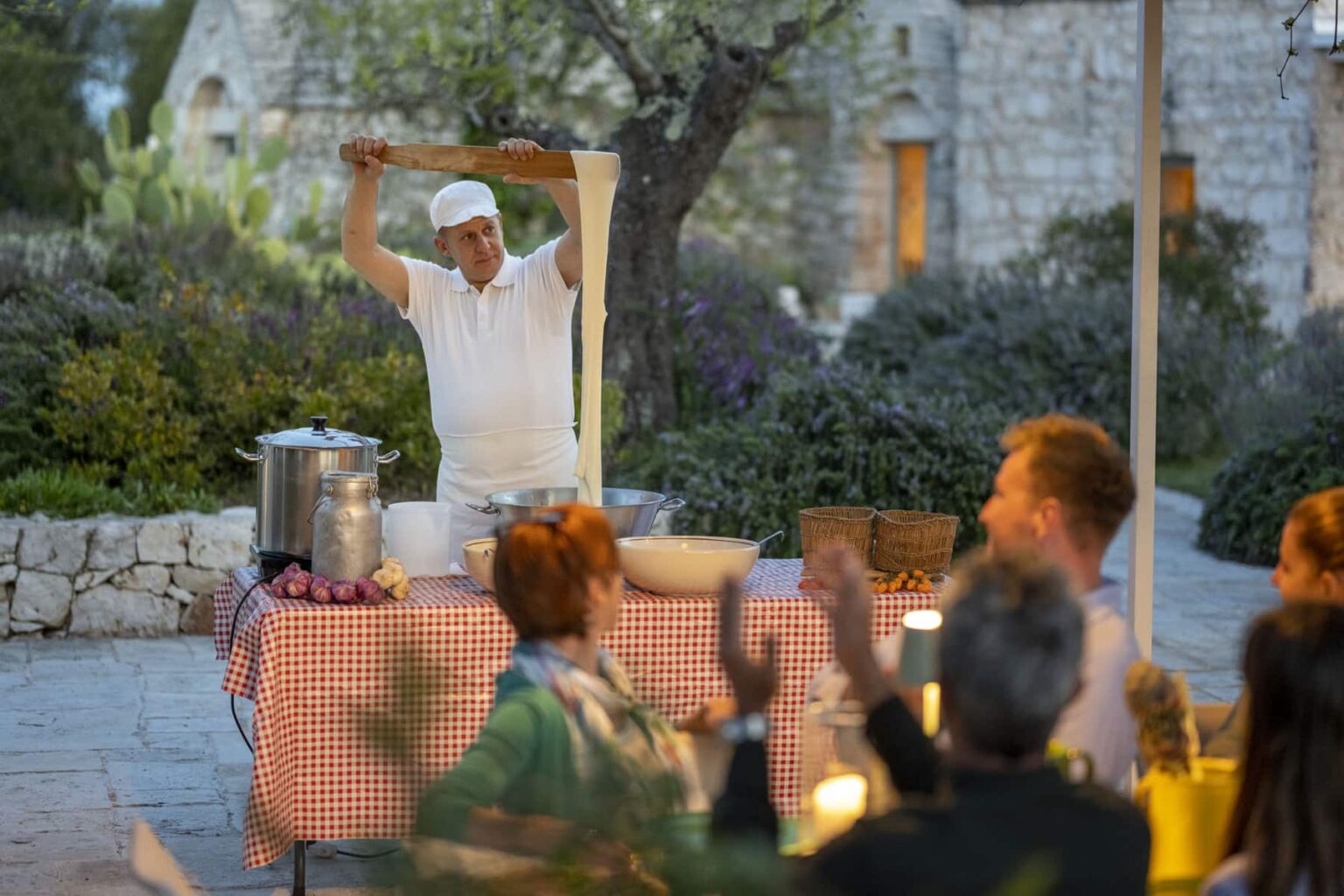 A chef performing a dough stretching demonstration at an outdoor dining event, with guests clapping and enjoying the culinary experience in a picturesque garden setting. | Only on SopranoVillas