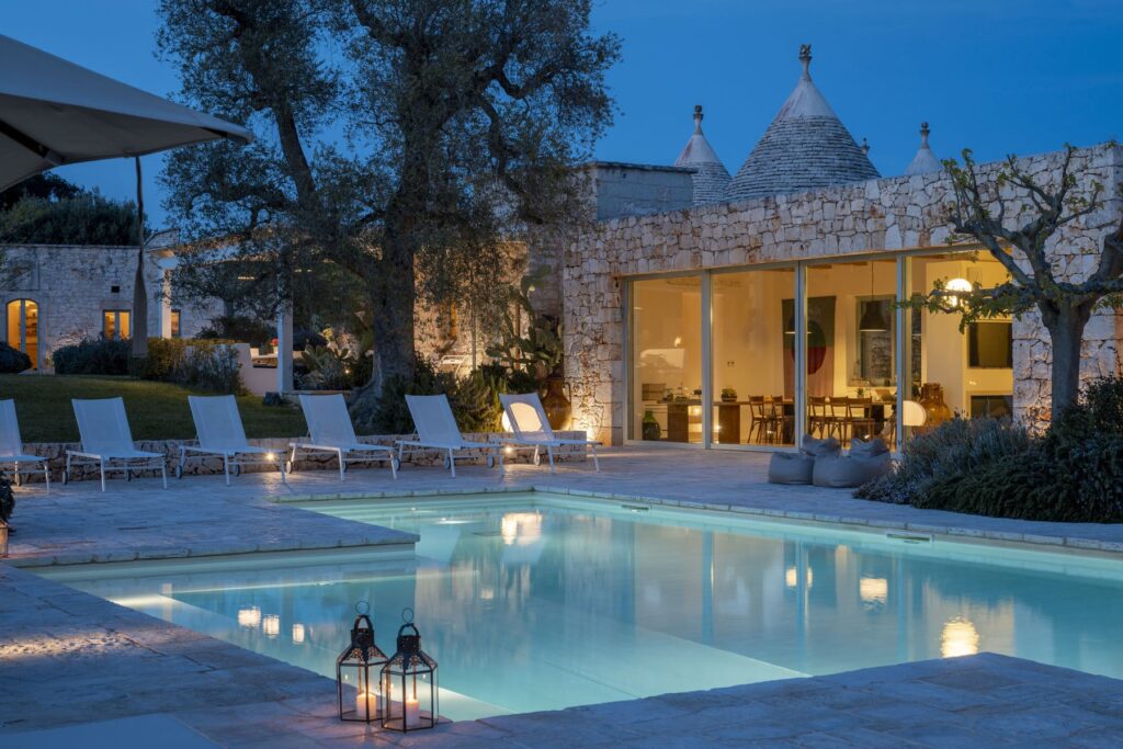 Luxury villa with a serene pool area illuminated at dusk, surrounded by stone architecture and lush greenery, ideal for relaxation and outdoor gatherings. | Only on SopranoVillas