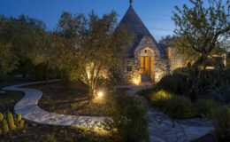 Charming stone cottage illuminated at dusk, featuring a winding pathway surrounded by lush greenery and soft lighting, creating an inviting atmosphere for evening strolls.