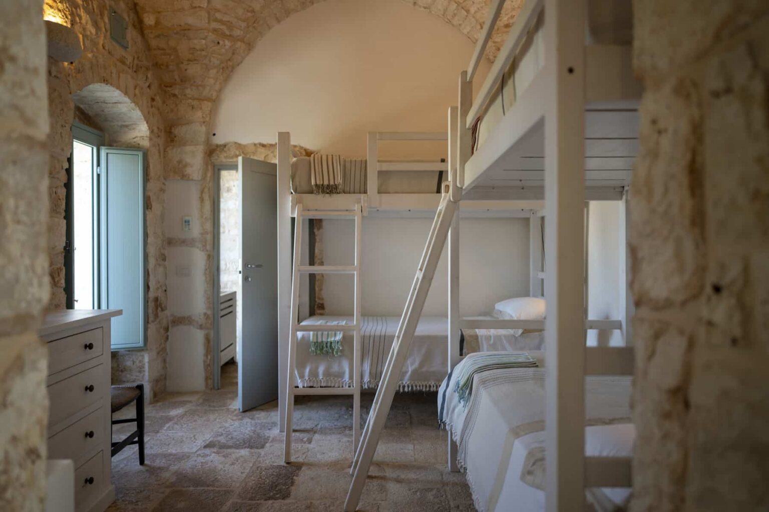 Cozy interior of a rustic bedroom featuring a wooden bunk bed, stone walls, and large windows allowing natural light, ideal for family stays or group accommodations. | Only on SopranoVillas