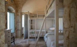 Cozy interior of a rustic bedroom featuring a wooden bunk bed, stone walls, and large windows allowing natural light, ideal for family stays or group accommodations.