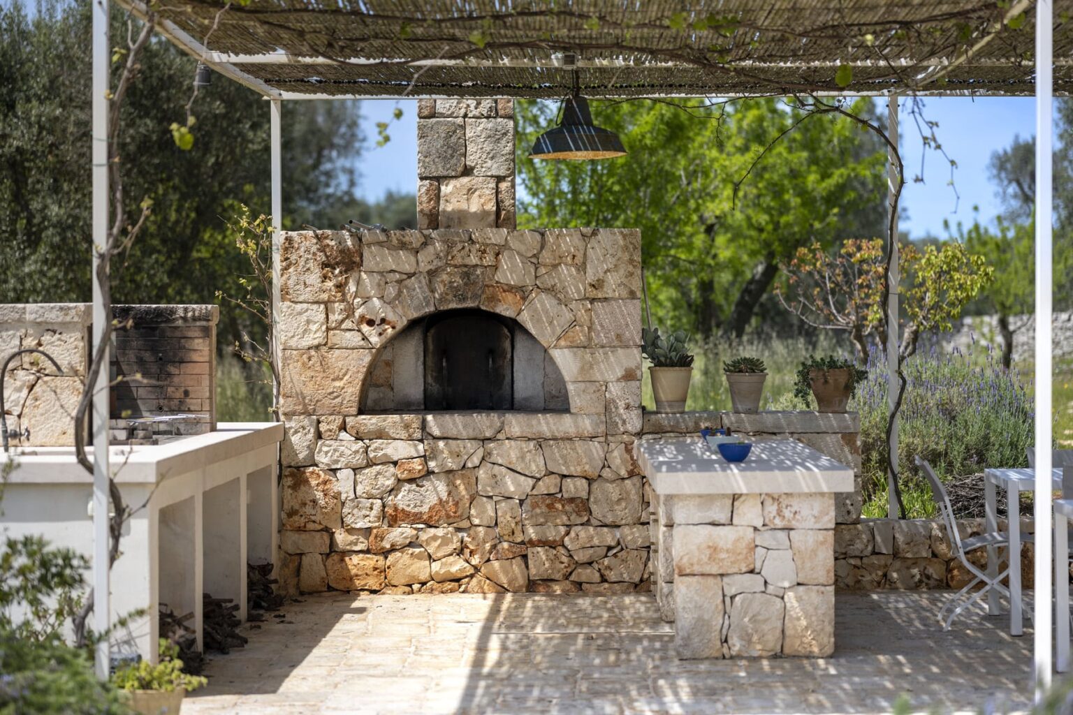 Outdoor stone kitchen featuring a traditional wood-fired oven, a spacious countertop, and surrounding greenery, ideal for grilling and entertaining. | Only on SopranoVillas