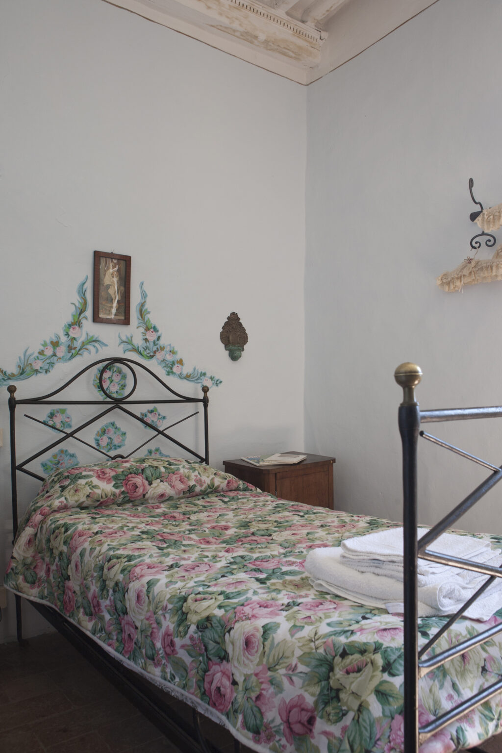 Cozy bedroom featuring a floral-patterned bedspread, decorative wall art, and a vintage wooden nightstand. The room has a charming, rustic ambiance with artistic wall decorations. | Only on SopranoVillas