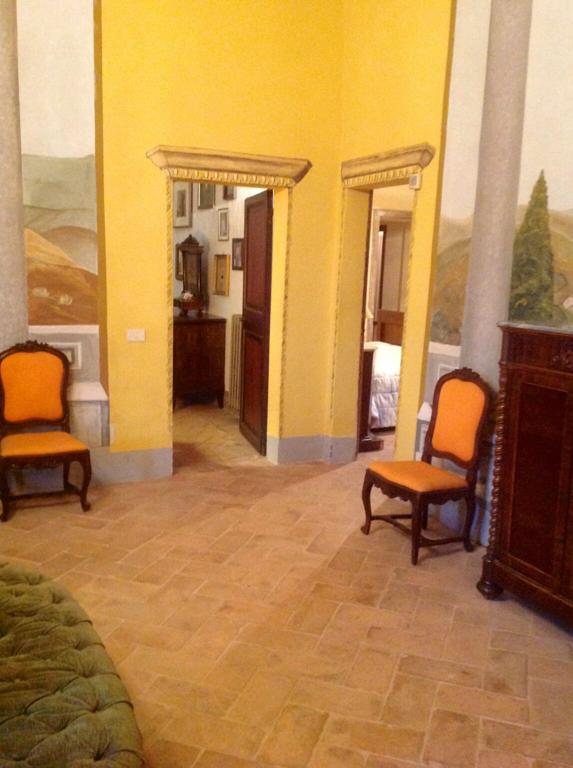 Interior view of a room featuring two vintage chairs with orange upholstery, a wooden cabinet, and a doorway leading to another area. The walls are painted in warm tones, and the floor is tiled, creating a cozy atmosphere. | Only on SopranoVillas