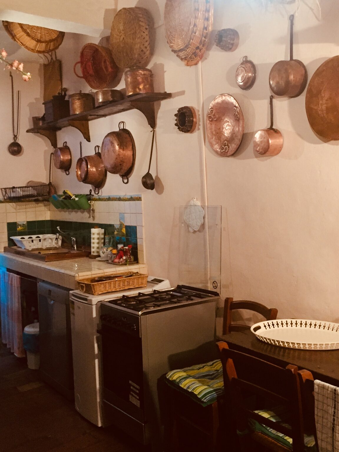 Cozy kitchen interior featuring a vintage stove, wooden furniture, and an array of copper pots hanging on the wall. The space is well-organized with a sink and colorful kitchen accessories, creating a warm and inviting atmosphere. | Only on SopranoVillas