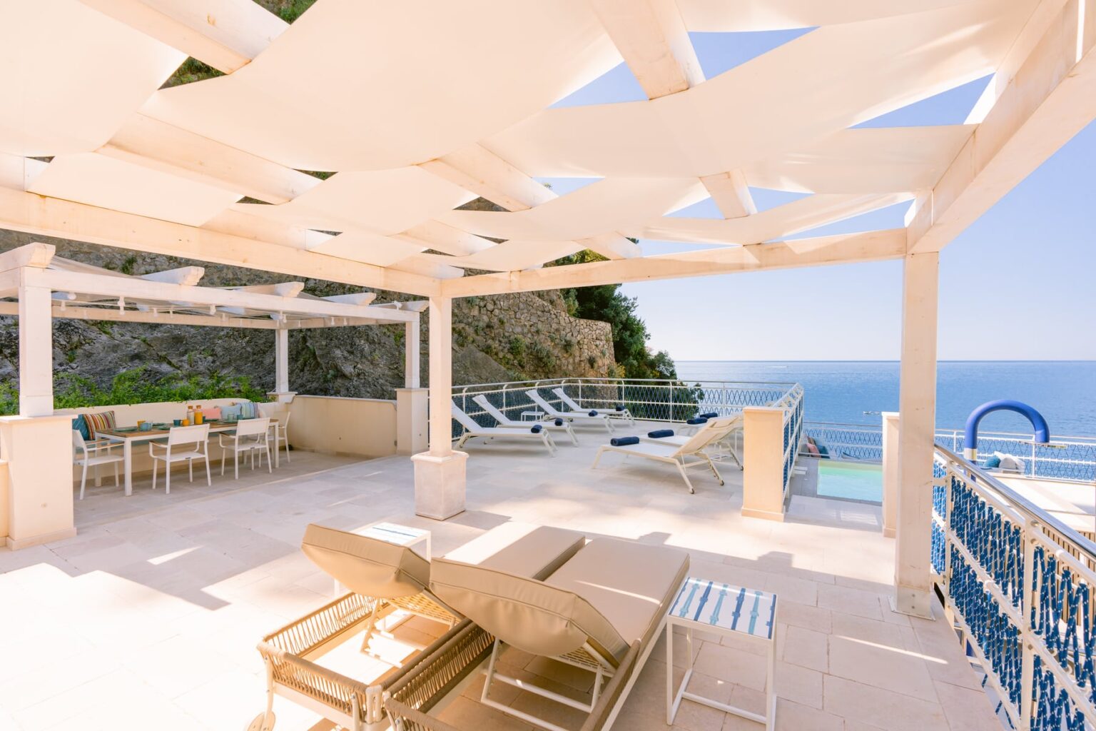 Luxury outdoor terrace with sun loungers and dining area overlooking the ocean, featuring a modern design and stunning coastal views. Ideal for relaxation and entertaining. | Only on SopranoVillas