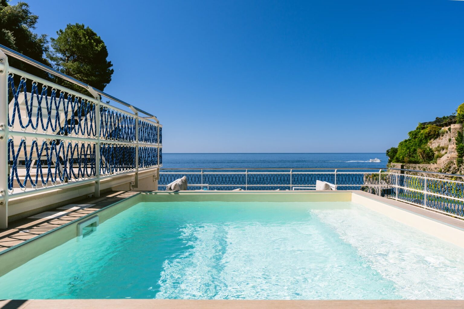 Luxury swimming pool with ocean view and clear blue sky, surrounded by a decorative railing and lush greenery, ideal for relaxation and vacation getaways. | Only on SopranoVillas
