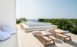 Modern outdoor terrace with a swimming pool, sun loungers, and a scenic ocean view, perfect for relaxation and leisure.