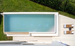 Aerial view of a modern swimming pool surrounded by lush green grass, featuring wooden lounge chairs and a stylish deck for relaxation.