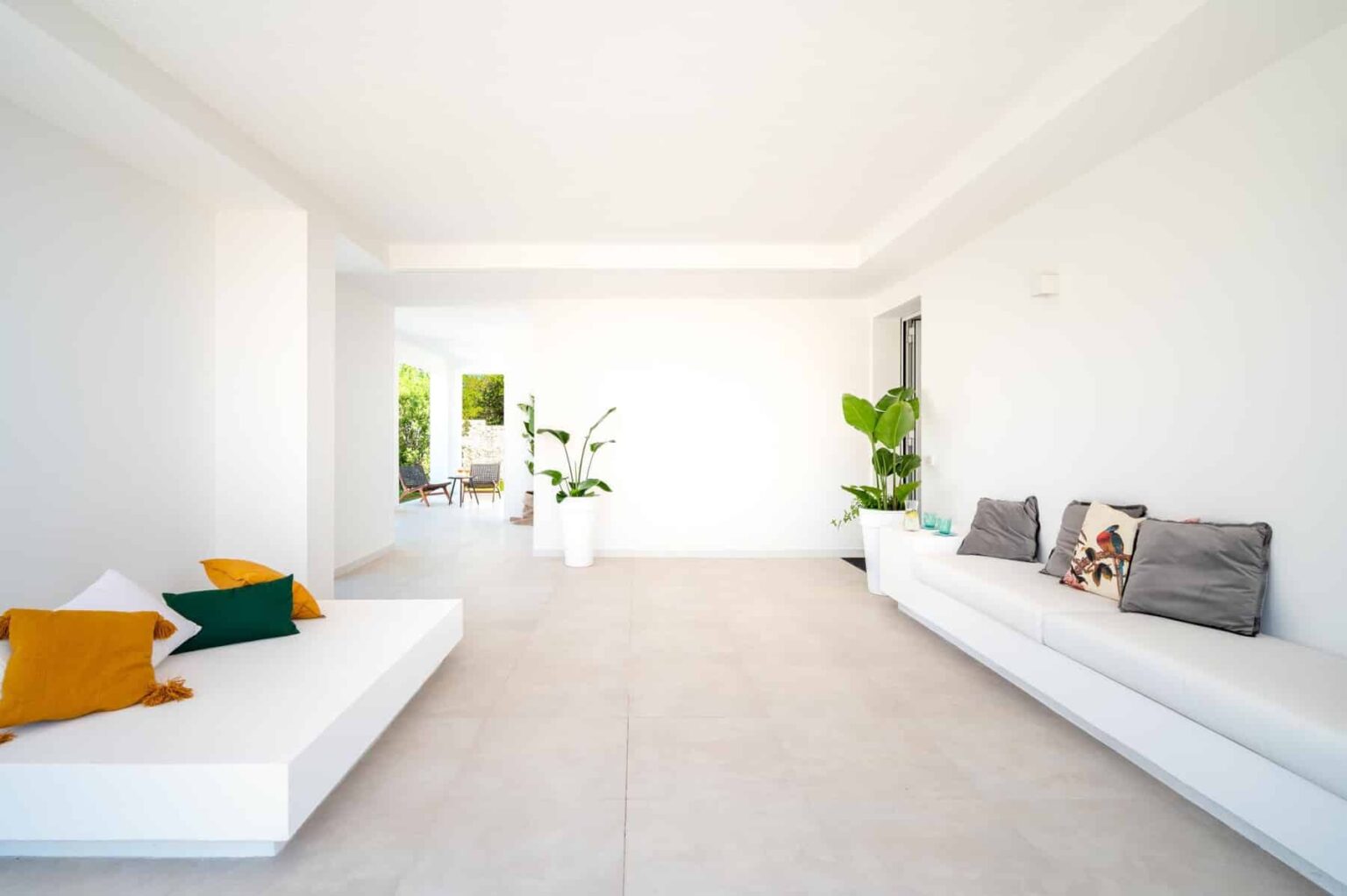 Spacious modern living room featuring white walls, minimalist furniture, and indoor plants, creating a bright and airy atmosphere. | Only on SopranoVillas