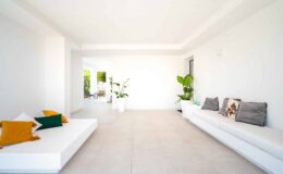 Spacious modern living room featuring white walls, minimalist furniture, and indoor plants, creating a bright and airy atmosphere.