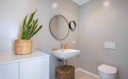 Modern bathroom interior featuring a sleek sink, round mirror, and minimalistic decor. A potted plant adds a touch of greenery, while neutral walls and stylish storage enhance the contemporary design. Ideal for home improvement inspiration.