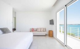 Modern beachfront bedroom with a large window showcasing ocean views, featuring a white bed, a cozy sofa, and minimalist decor.