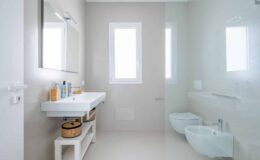 Modern bathroom design featuring a minimalist aesthetic, white walls, natural light from windows, a sleek vanity with toiletries, and stylish storage baskets.