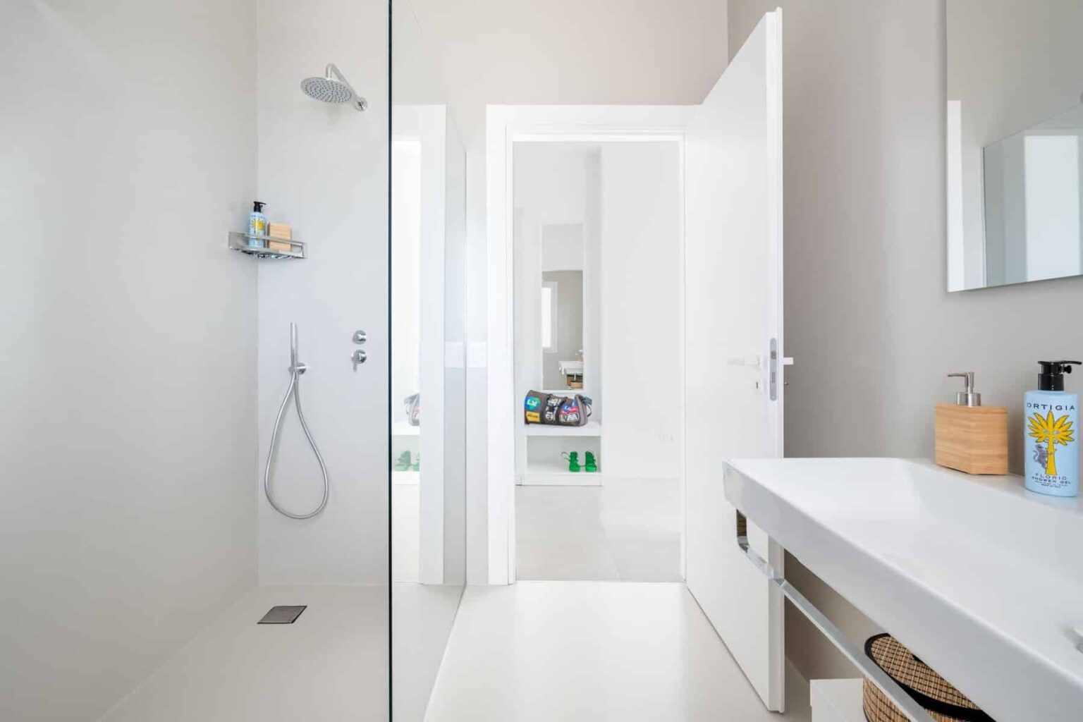 Modern bathroom interior featuring a glass shower enclosure, sleek white walls, and a minimalist vanity with a sink and storage. Natural light illuminates the space, highlighting the clean lines and contemporary design. | Only on SopranoVillas