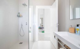 Modern bathroom interior featuring a glass shower enclosure, sleek white walls, and a minimalist vanity with a sink and storage. Natural light illuminates the space, highlighting the clean lines and contemporary design.
