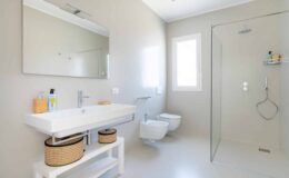 Modern bathroom design featuring a sleek white vanity with a large mirror, minimalist shower enclosure, and natural light from a window. The space includes a contemporary toilet and stylish storage baskets, showcasing a clean and functional aesthetic.