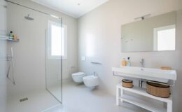 Modern bathroom featuring a glass shower, minimalist design, a wall-mounted sink with a wooden storage basket, and a large mirror, all set against neutral-colored walls.