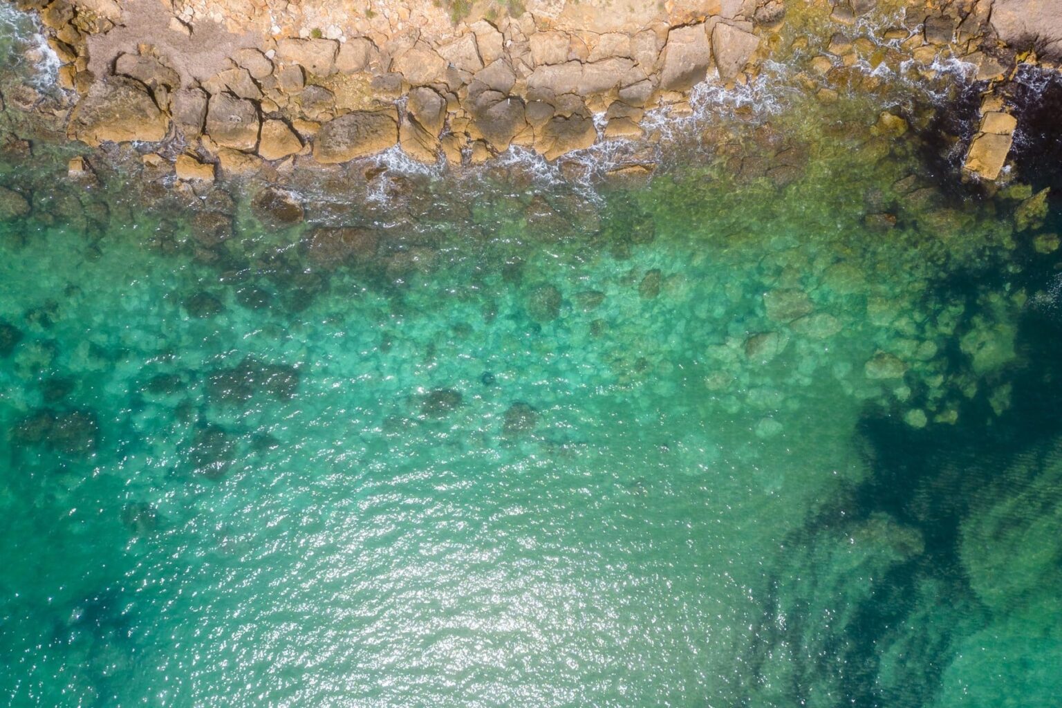 Aerial view of a rocky coastline with clear turquoise waters, showcasing the contrast between land and sea, ideal for nature enthusiasts and beach lovers. | Only on SopranoVillas