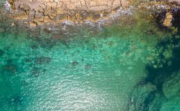 Aerial view of a rocky coastline with clear turquoise waters, showcasing the contrast between land and sea, ideal for nature enthusiasts and beach lovers.