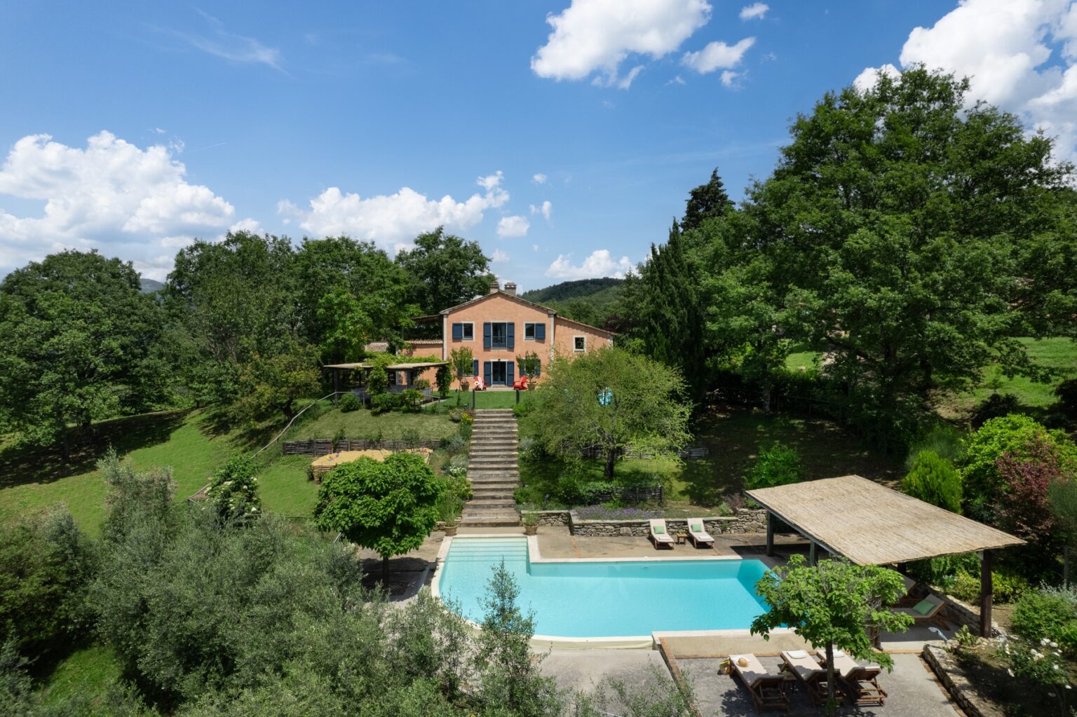 Aerial view of a beautiful countryside villa featuring a swimming pool, landscaped gardens, and lush greenery under a clear blue sky. | Only on SopranoVillas