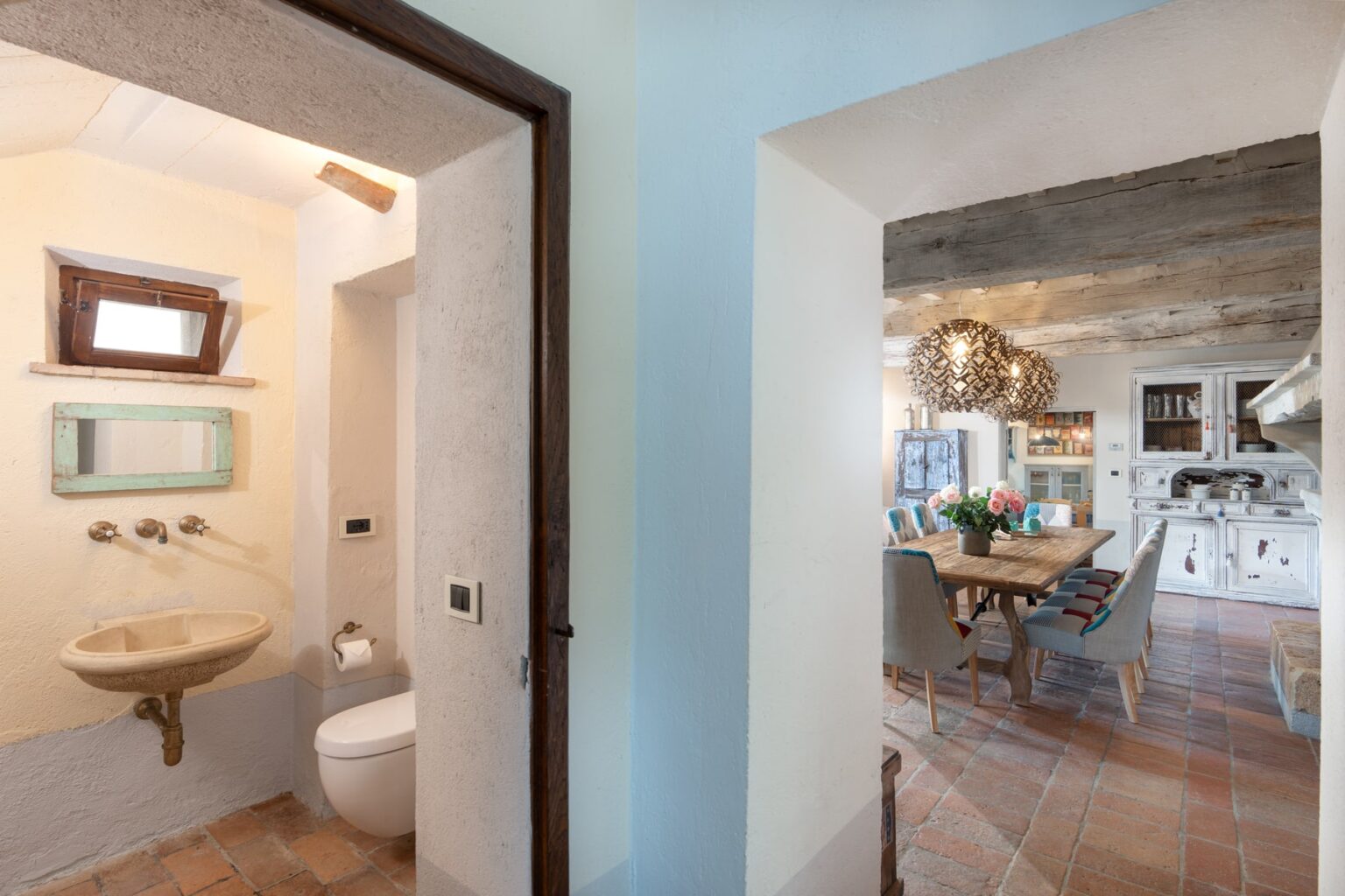 Interior view of a modern home showcasing a small bathroom with a sink and toilet on the left, and an open dining area with a kitchen on the right, featuring stylish decor and natural lighting. | Only on SopranoVillas