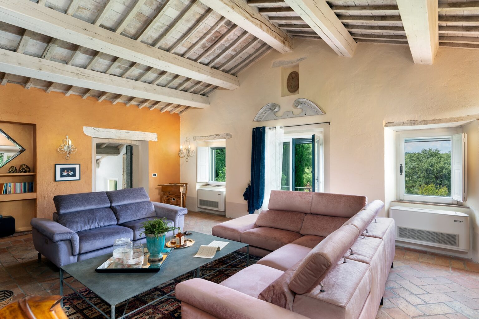 Spacious and inviting living room featuring modern sofas, a coffee table with decor, large windows with scenic views, and rustic wooden beams on the ceiling, perfect for relaxation and entertaining. | Only on SopranoVillas