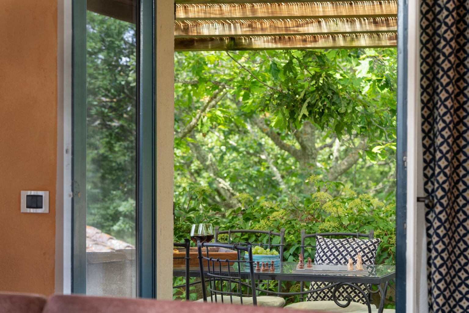 Cozy indoor view showcasing a patio with a small table and chairs, surrounded by lush greenery and a thatched roof overhang, inviting a serene outdoor dining experience. | Only on SopranoVillas