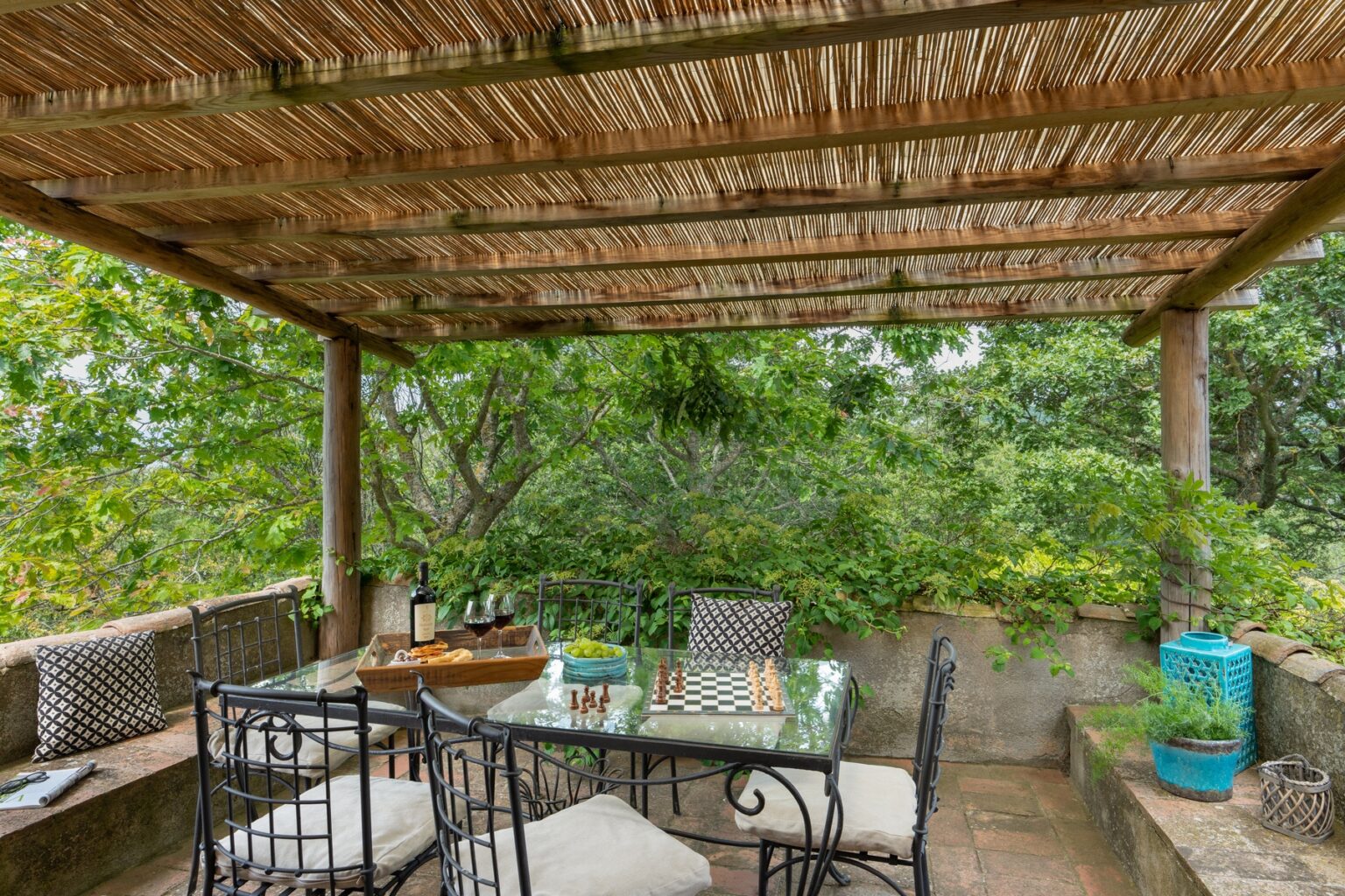 Outdoor dining area with a thatched roof, featuring a rustic table and chairs surrounded by lush greenery. Ideal for enjoying meals in a natural setting. | Only on SopranoVillas
